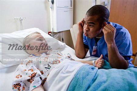 Hospital worker sitting by young boy in hospital bed