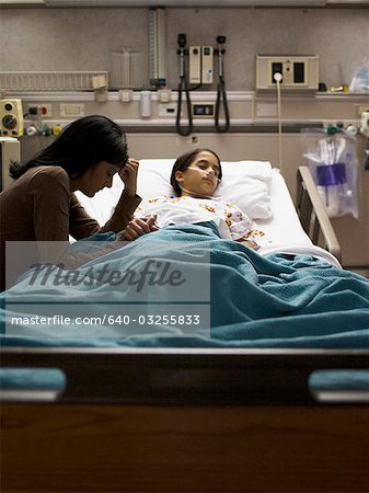 Mother sitting nervously by daughter in hospital bed