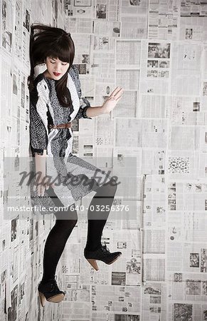Jeune femme tomber un mur recouvert de journaux, studio shot