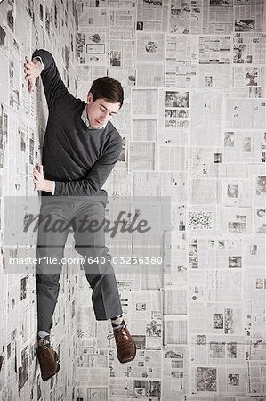 Young man stuck to wall covered with newspapers, studio shot