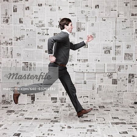 Young man running in front of wall covered with newspapers