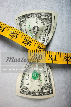 Studio shot of yellow measure tape squeezing two one dollar bills