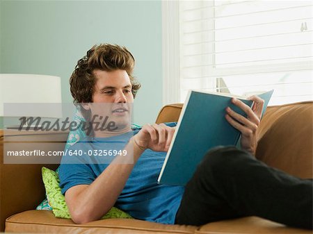 USA, Utah, Provo, young man lying down on sofa and reading book