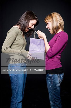 Young woman giving friend gift bag, studio shot