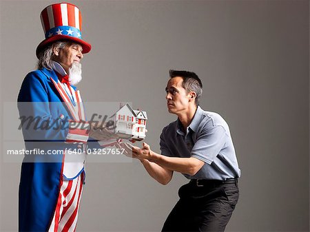 Man in Uncle Sam's costume giving model of house to other man, studio shot