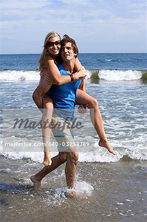 Man carrying woman through shallow water at the beach