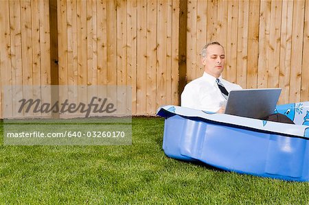 Kaufmann in einem Hinterhof-Pool auf einem laptop