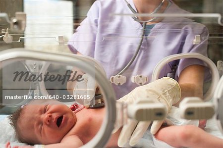 Nurse examining newborn in incubator