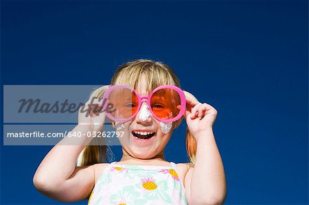 Girl with suntan lotion and sunglasses smiling with arms up