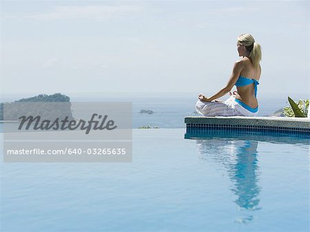 Vue arrière d'une femme adulte moyenne assis dans une position de lotus au bord de la piscine