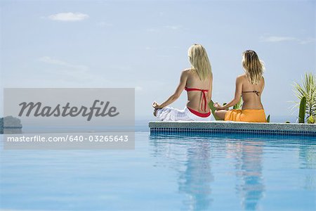Vue arrière d'une jeune femme et une femme adulte moyenne assis dans une position de lotus au bord de la piscine