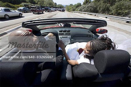 Vue arrière d'un couple de jeunes mariés dans une voiture décapotable