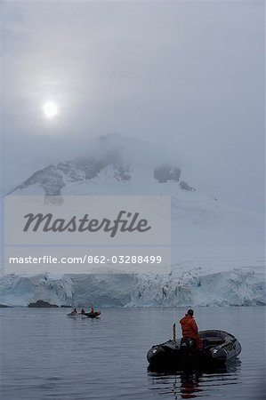 L'Antarctique, la péninsule Antarctique, Paradise Harbour. Un pilote de bateau de zodiaque depuis le navire de l'expédition Discovery MV flotte sur les eaux protégées de Paradise Harbour comme le matin soleil brise à travers le nuage de tôt le matin.