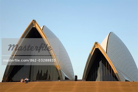Un couple assis sur les marches de l'opéra sont rabougris par les toits arqués iconiques