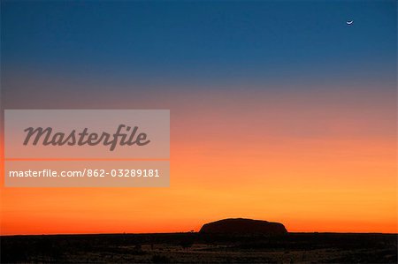 Australie, Northern Territory. Avant le lever du soleil, Uluru ou Ayres Rock est silhouetté sur un magnifique rouge sang à ciel orange. Cette image est extraite de The Olgas, à 16 km de la caractéristique phare.