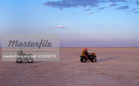 En fin d'après-midi, visiteurs traversent les salines de Ntwetwe sans relief de quadricycle. Ntwetwe est à l'ouest des deux salines énormes, qui composent l'immense région de Makgadikgadi du Kalahari du Nord parmi les plus grandes étendues de marais salants dans le monde.