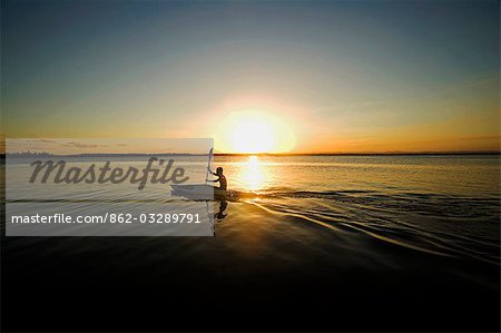 Brasilien, Bahia, Barra de Serinhaem. Junger Mann Kanu bei Sonnenuntergang.
