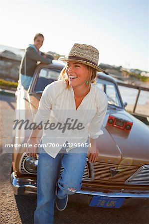 Frau sitzt auf der Motorhaube eines Autos Vintage am Strand, Santa Cruz, Kalifornien, USA