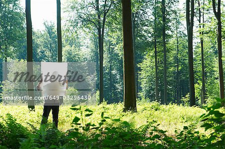 Man in the woods, looking at blueprint