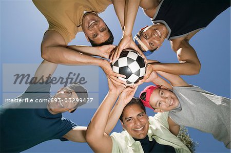Garçon (13-15) avec les frères et le père tenant le ballon ensemble, vue de dessous.