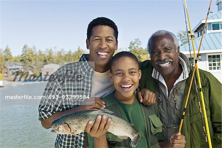 Male members of three generation family showing fish, smiling, (portrait)