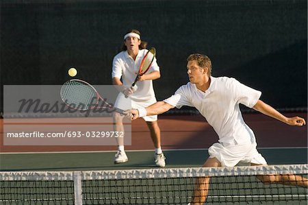 Tennis Player stretching, Swinging at Ball near tennis net, doubles partner standing behind