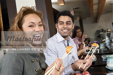 Young people eating sushi with chopsticks in restaurant