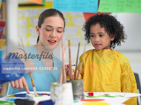 Professeur d'arts plastiques accroupi à côté de la fille de peinture dans la classe d'art
