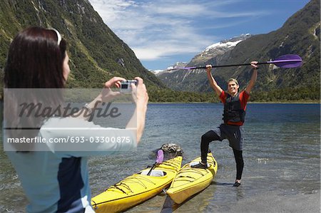 Femme prise de photo d'homme rame de kayak de levage sur la tête sur la rive du lac de montagne