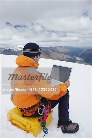 Hiker using laptop on snowy mountain peak, back view