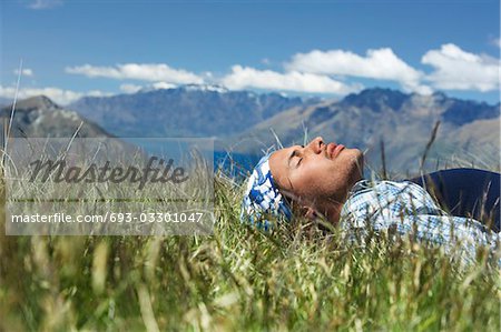 Man lying in field by lake and hills