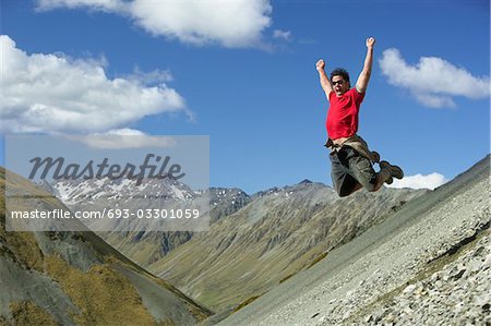 Man jumping down rocky slope with arms raised