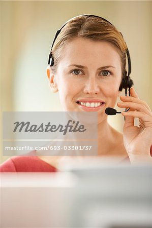 Mid-adult female office worker sitting in cubicle wearing headset, portrait