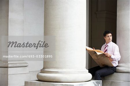 Businessman sitting on pillar under entablature reading newspaper