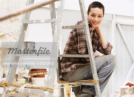 Female interior decorator sitting on ladder in work site, portrait