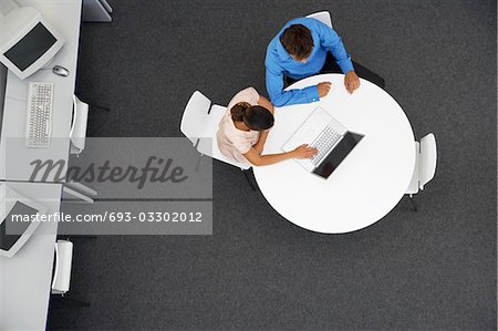 Man and Woman sitting at table using laptop in computer room, overhead view