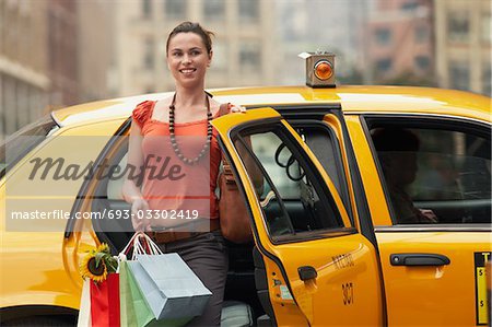 Young woman with shopping bags exiting yellow taxi cab