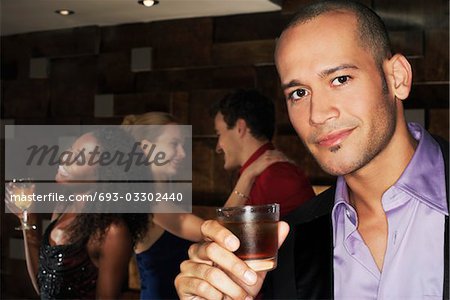 Young man holding drink, standing in bar, portrait