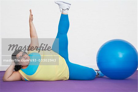 Femme couchée par ballon d'exercice s'étirant les bras et la jambe vers le haut en surpoids