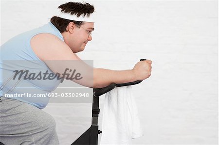 Homme obèse sur vélo d'appartement, vue latérale