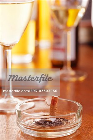 Cigarette in ashtray on table with glasses of wine