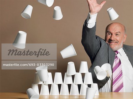 Businessman knocking down pyramid of plastic cups
