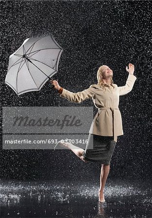 Woman standing on one leg, holding umbrella, leaning into falling rain
