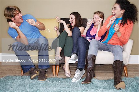 Young women throwing popcorn at friend on sofa