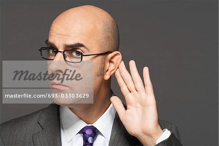 Balding man with hand behind ear, listening closely