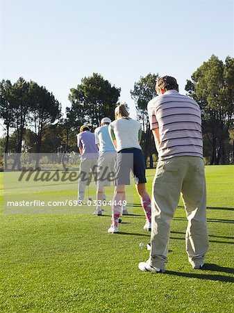 Golfers teeing off, back view