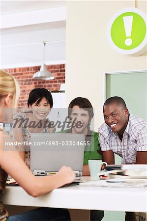 Four people having meeting around laptop, laughing.