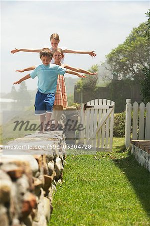 Three children (5-6, 7-9,10-12) walking in row on stone wall