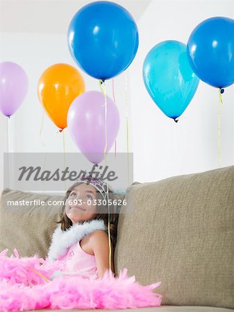 Young girl (7-9) sitting on sofa looking at balloons