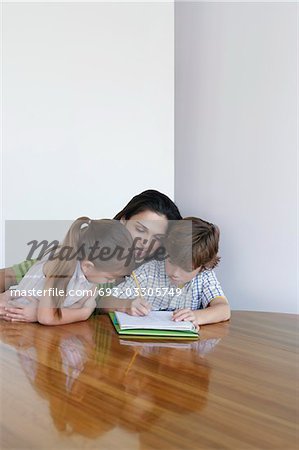 Mother assisting son (7-9) and daughter (5-6) doing homework